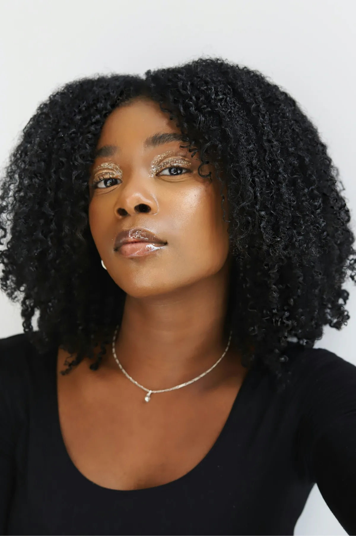 A photo of a model wearing gold eyeshadow looks softly at the camera.